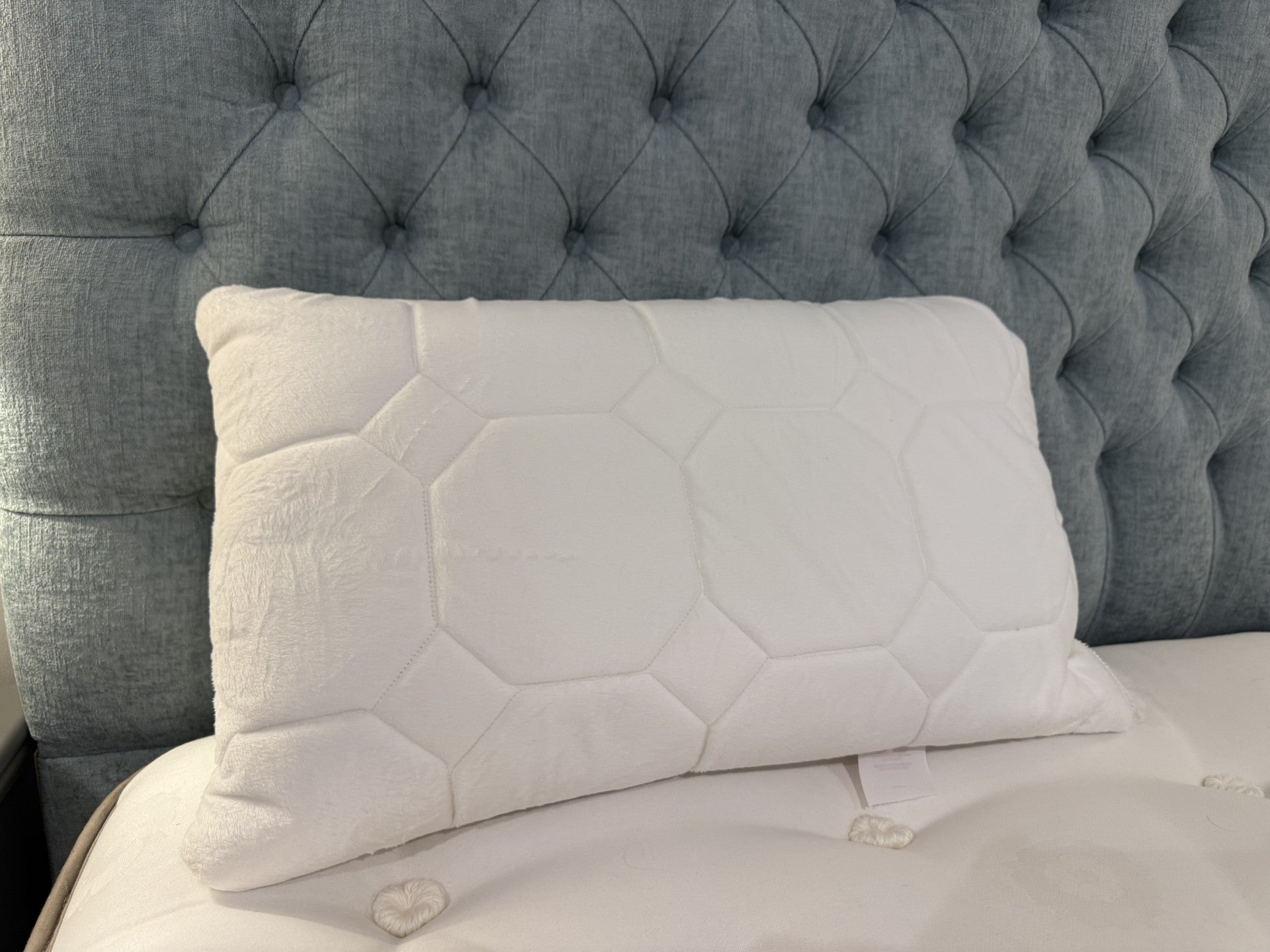 White quilted pillow on a bed with a tufted gray headboard