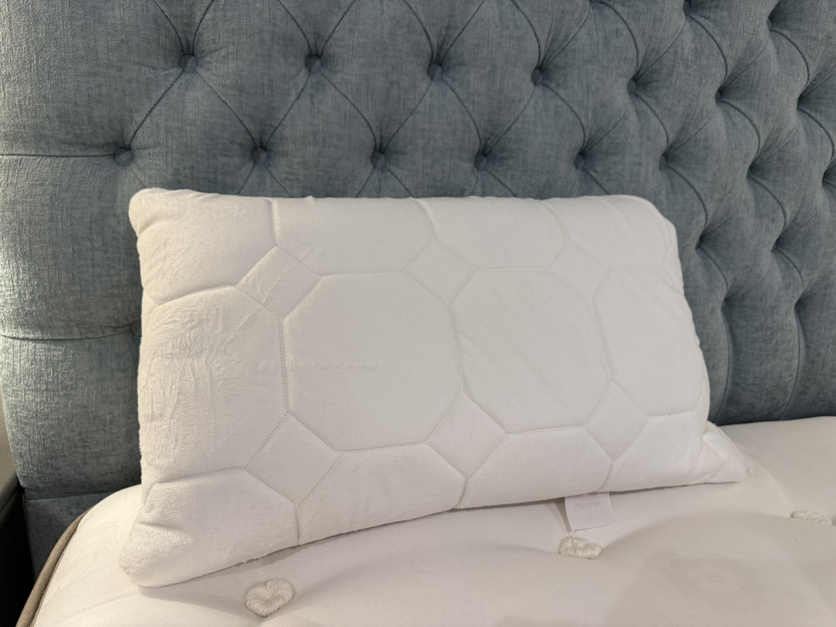 White quilted pillow on a bed with a tufted gray headboard